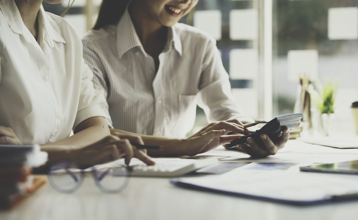 two women holding calculator and other materials at work desk