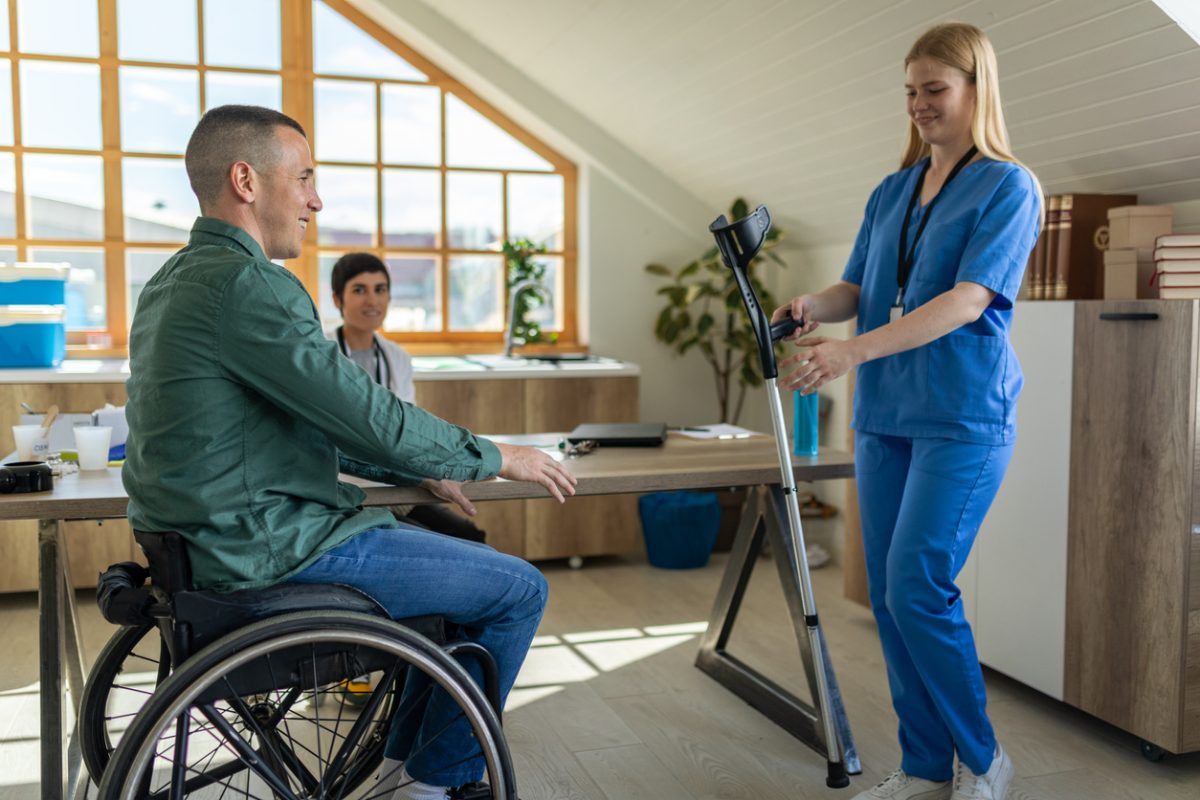 A young adult handing a disabled man crutches in a doctor's office