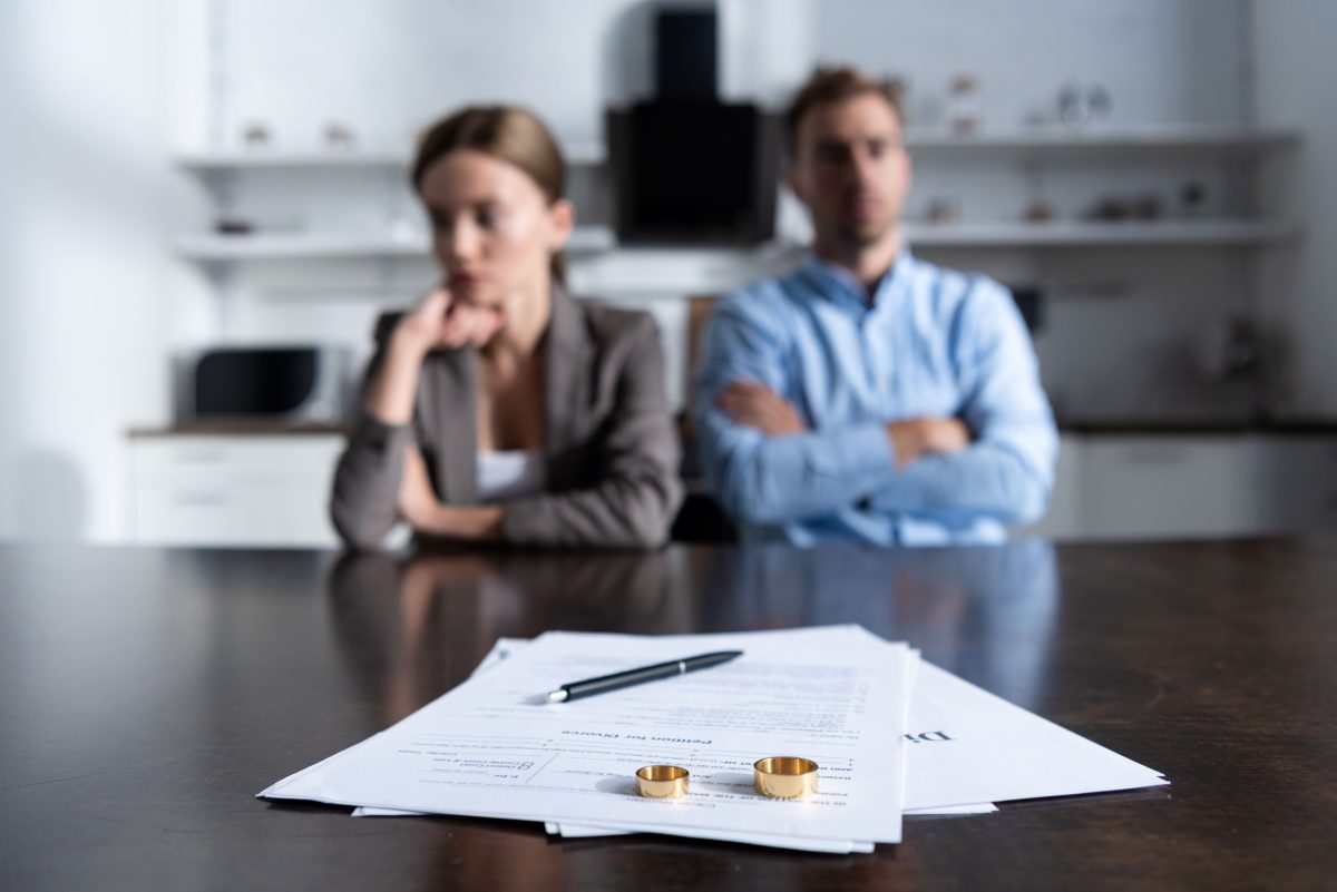 man and woman sitting at a table with divorce papers, a pen and two wedding bands