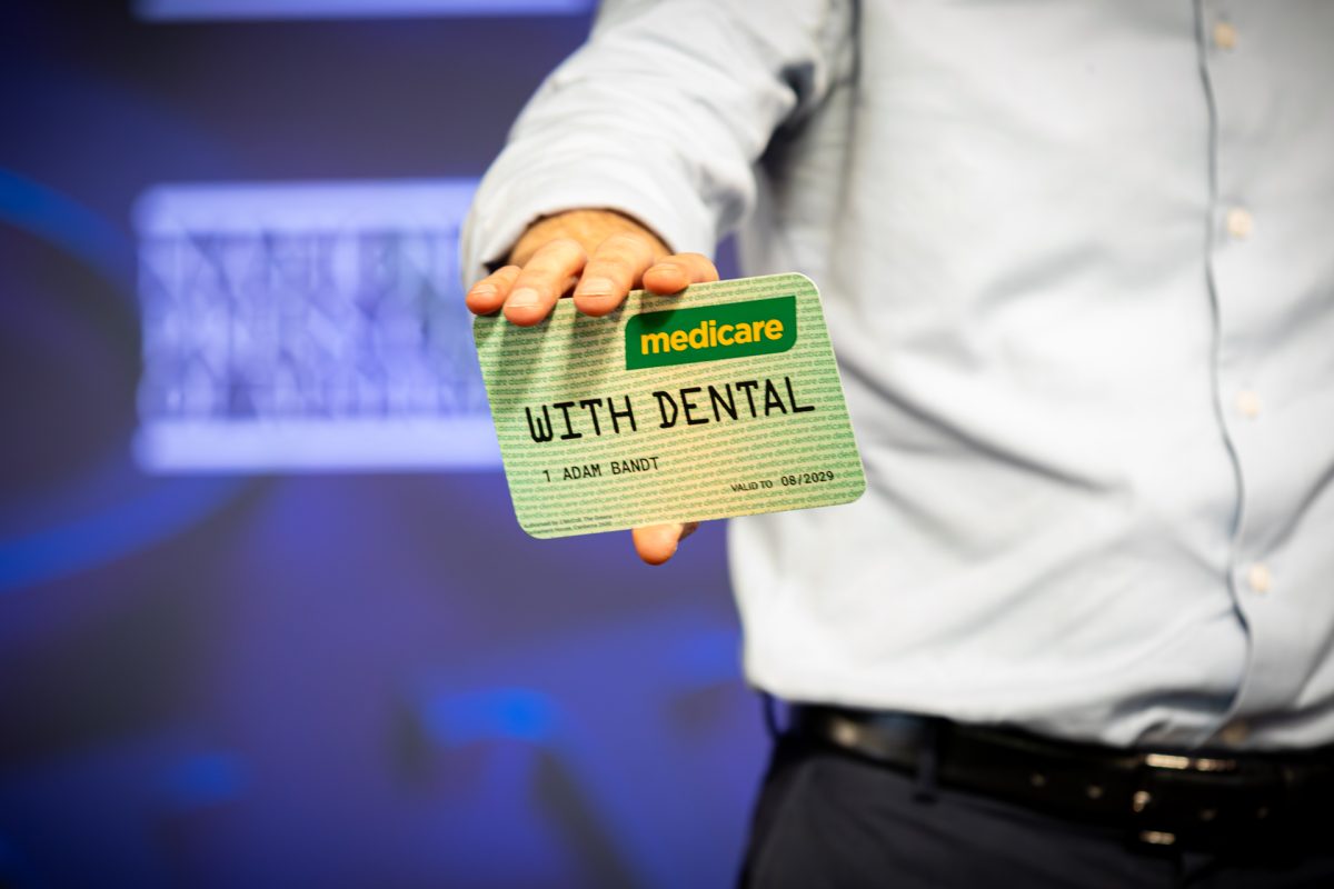 Man holding a mock up of a Medicare card 'WITH DENTAL' written on it.