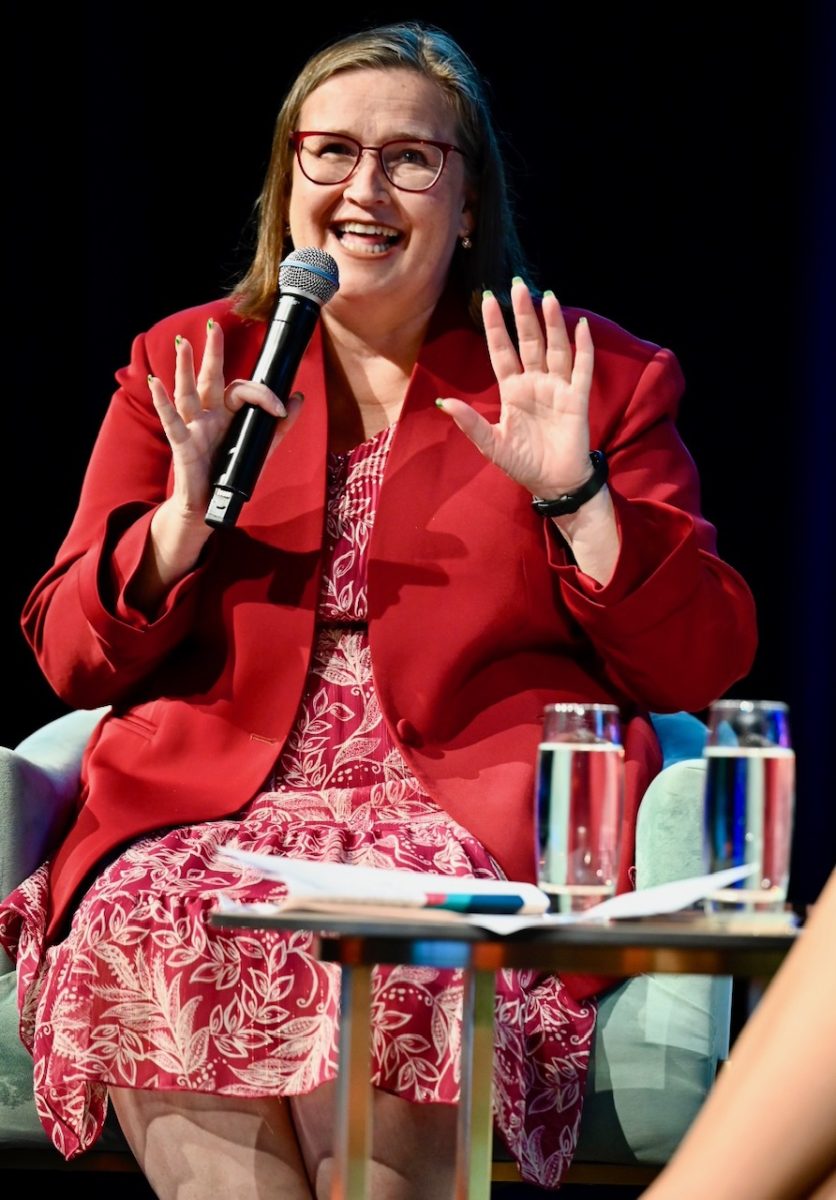 Wonan in red coat holding a microphone.