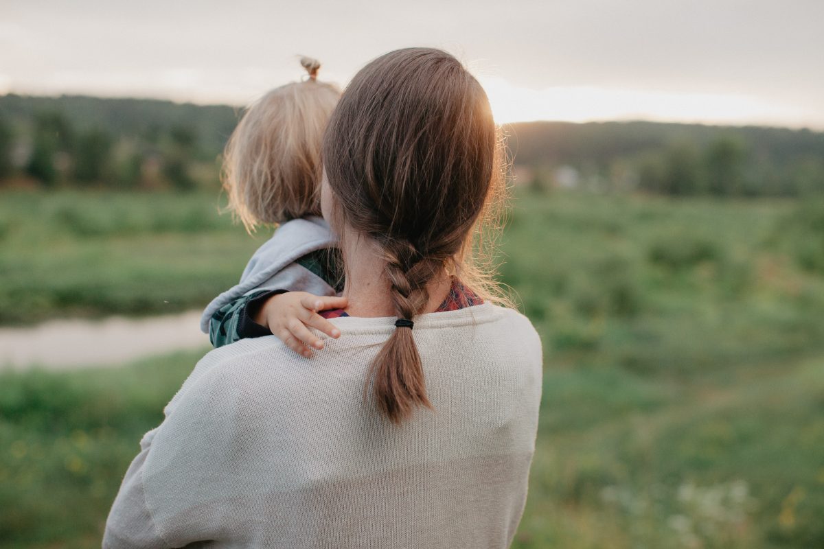 woman with baby photographed from behind gazing at hills at sunset