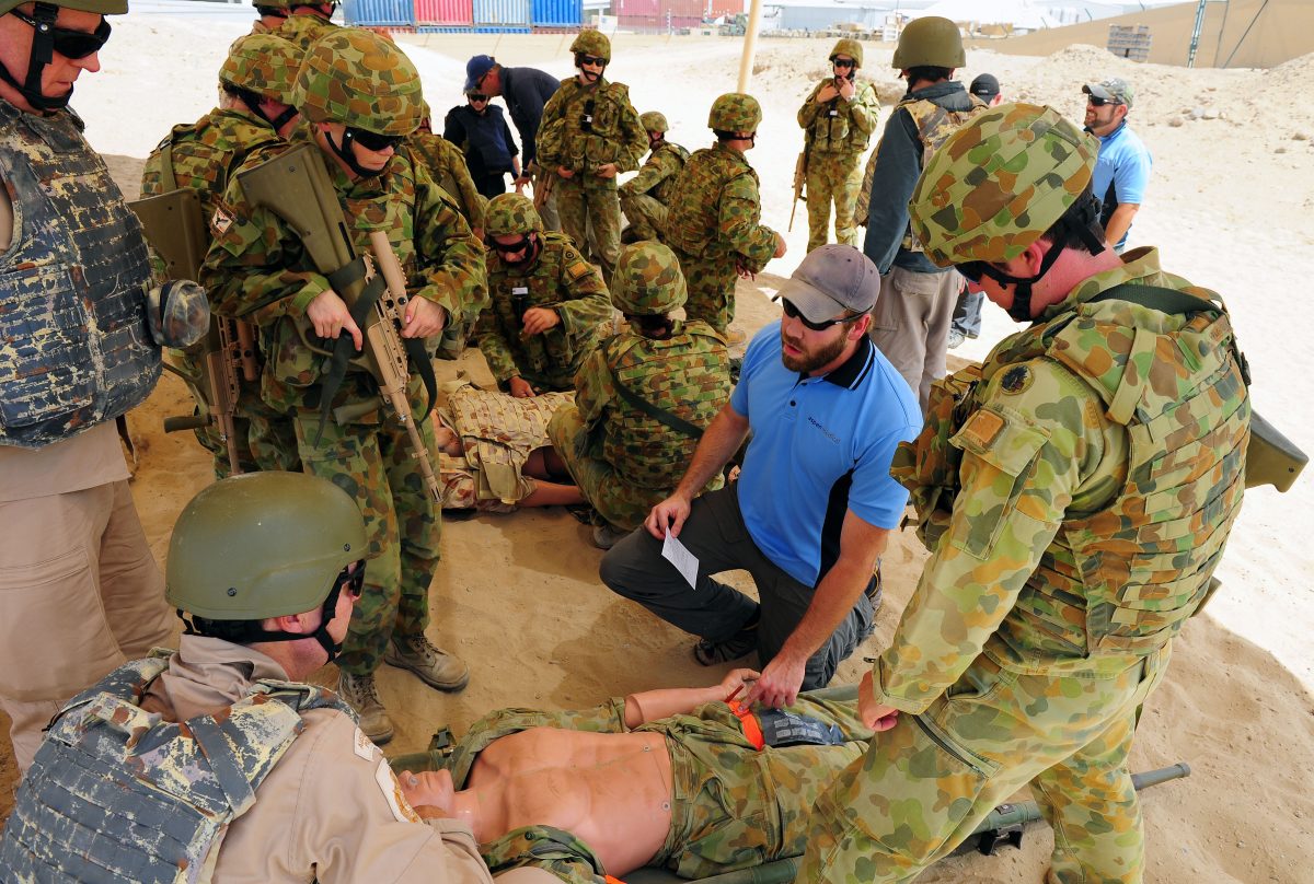 Soldiers crowd around a first aid dummy as a medical practitioner prepares to demonstrate CPR