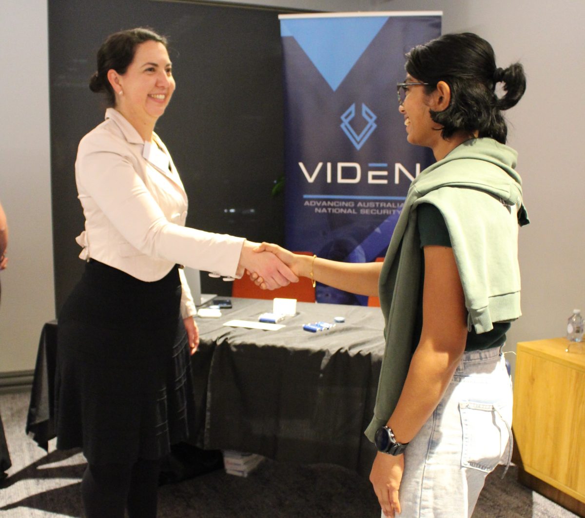 two women smiling and shaking hands with Viden sign in the background.