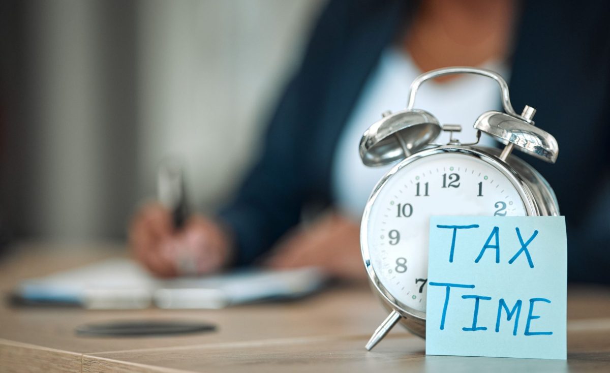 alarm clock with tax time on post-it note and woman writing in background