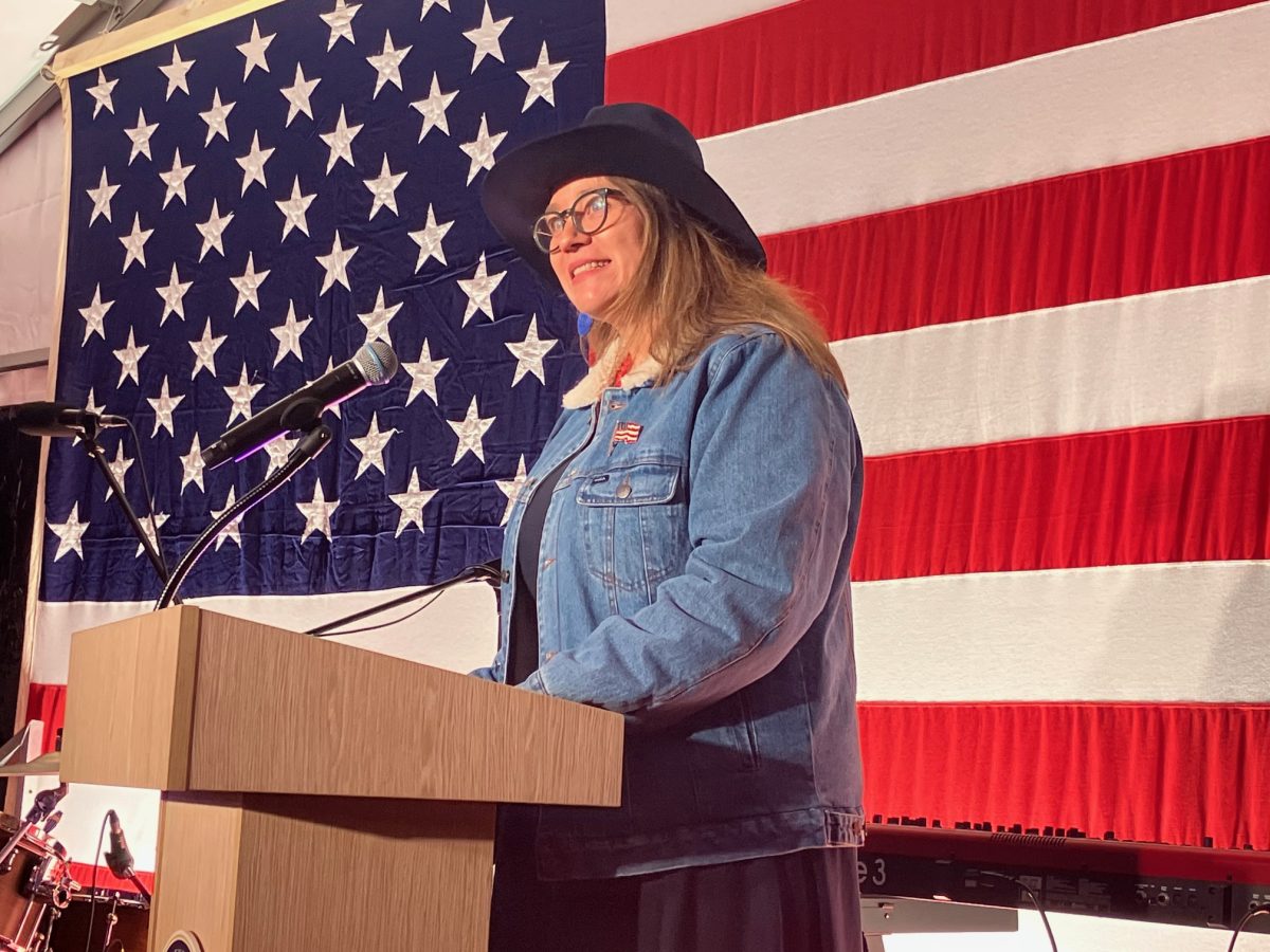 A woman wearing a cowboy hat while standing at a lectern in front of an American flag
