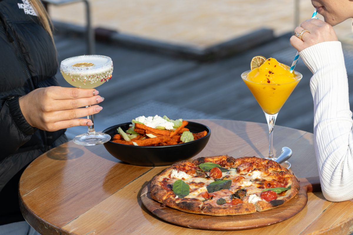 Two people drinking cocktails and eating pizza and chips