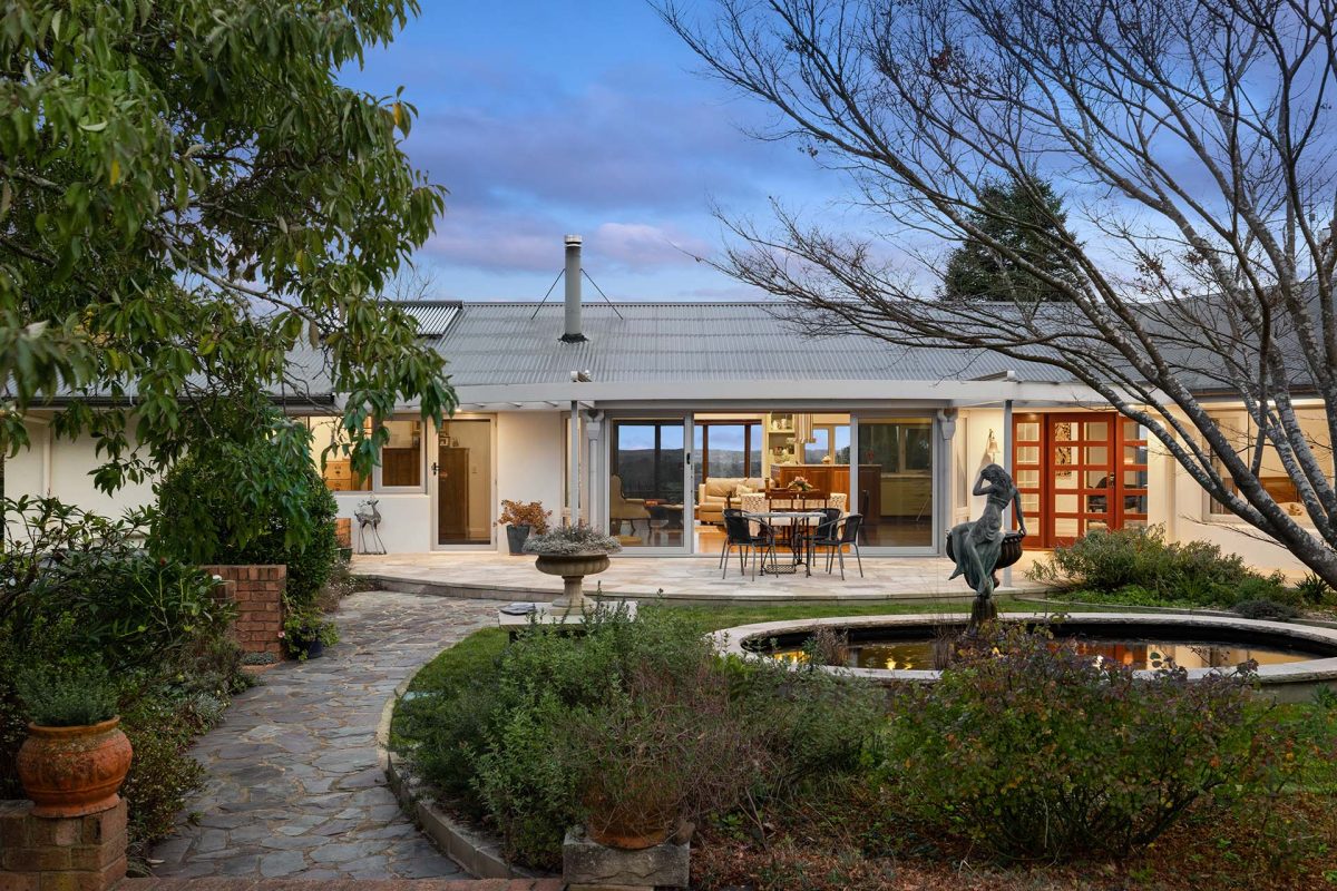 landscaped path leading past water feature to modern home at dusk