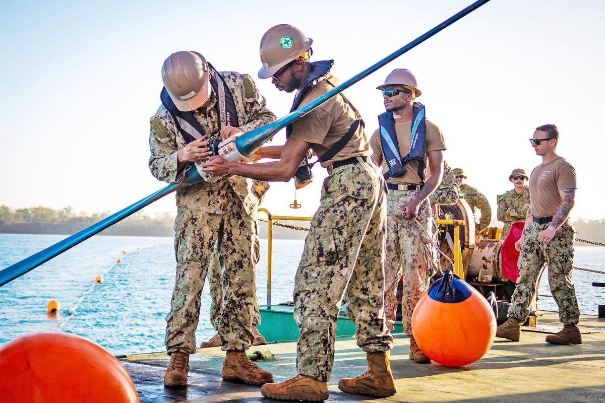 Seaman Boatswain's Mate Qwante Huggins, right, and Boatswain's Mate 3rd Class Joshua Banks, both assigned to Amphibious Construction Battalion 1, work together to affix the buoy connector aboard the commercial Australian vessel Bandicoot during Talisman Sabre 23 in Weipa.