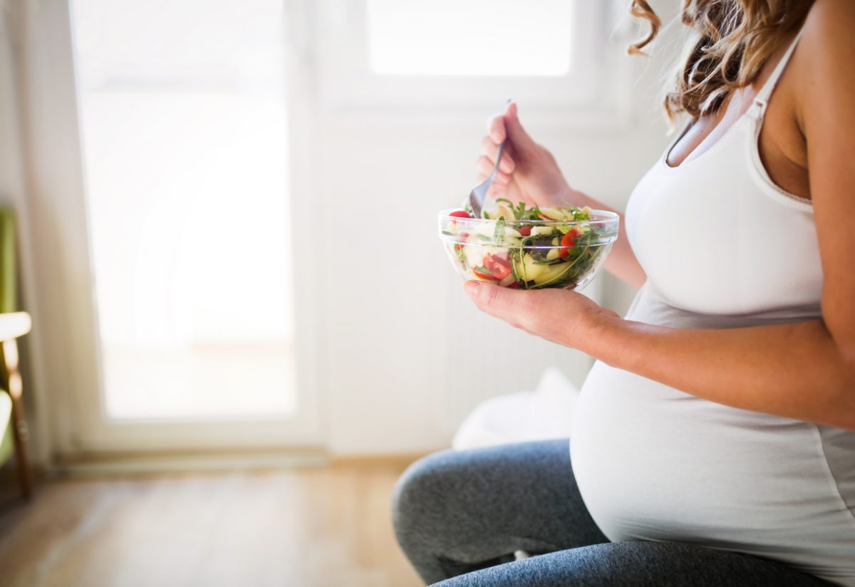 pregnant woman eating a bowl of salad