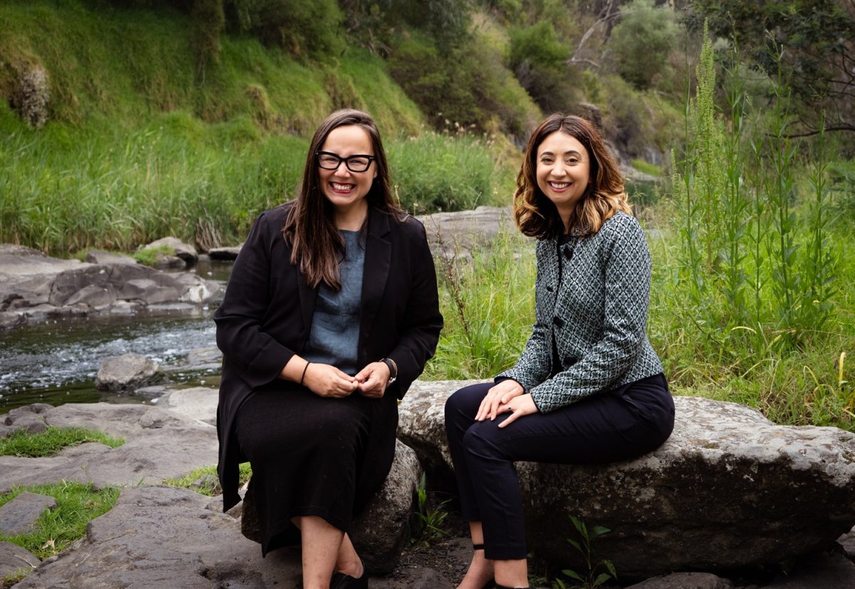 two women sitting on a rock next to a river