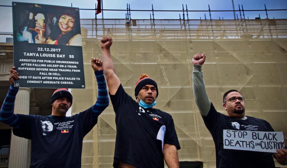 Three protestors standing outside Victoria's parliament with a sign about Tanya and one stating 'Stop Black Deaths in Custody'.