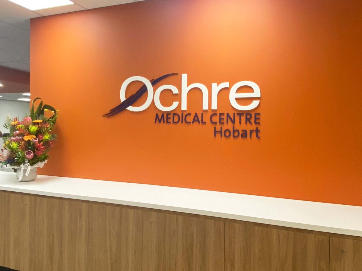 The entrance to the Ochre Medical Centre in Hobart, with an orange wall and sign of the logo up on it.
