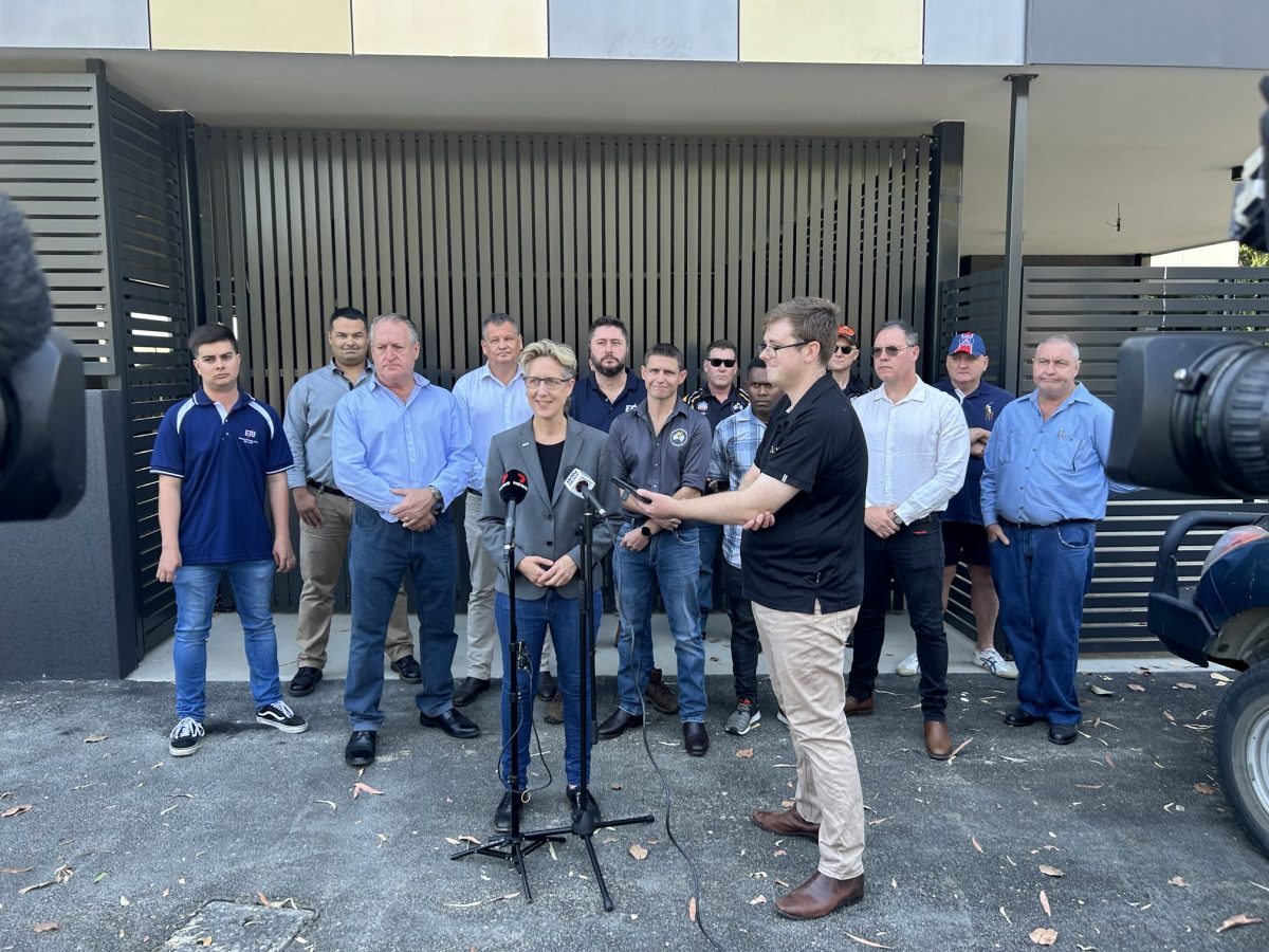 Sally McManus in front of microphones and cameras with a group of unionists behind her.