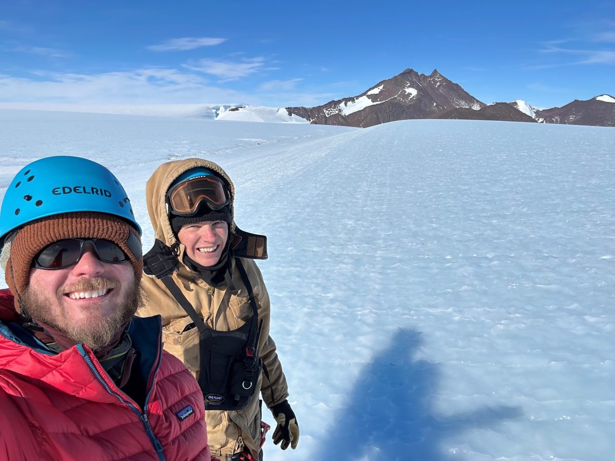 Scott and Jess standing in the snow with a mountain behind them in Antarctica.