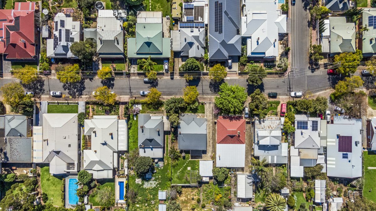 Aerial view of leafy eastern suburban houses either side of T-intersection in Adelaide, South Australia: directly above, rooftop solar, front & backyard, play equipment, variety of roofing materials and colours; motor vehicles; swimming pool.