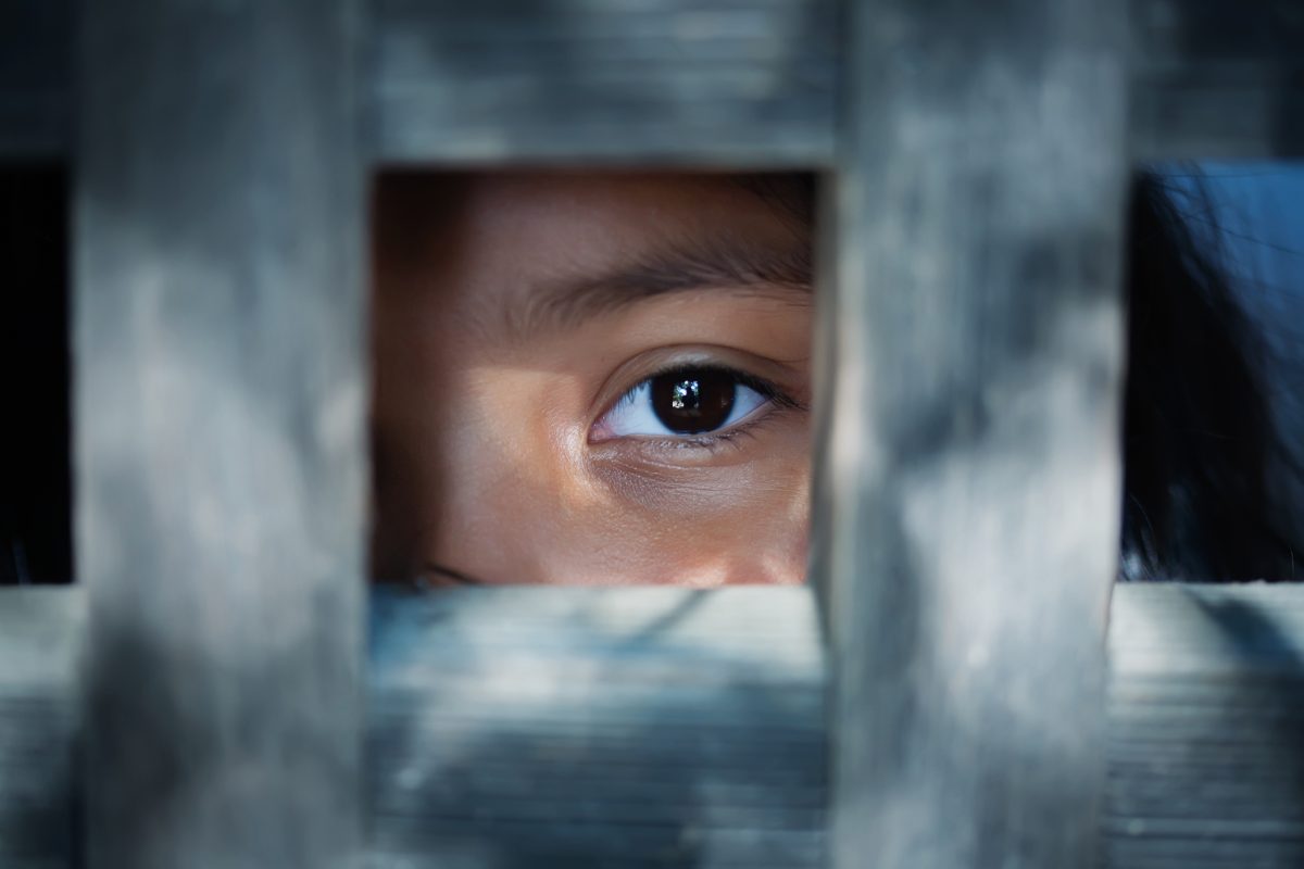 The blank stare of a child standing behind what appears to be a wooden door frame