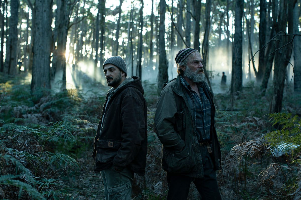 still from a movie, with two men standing in a forest