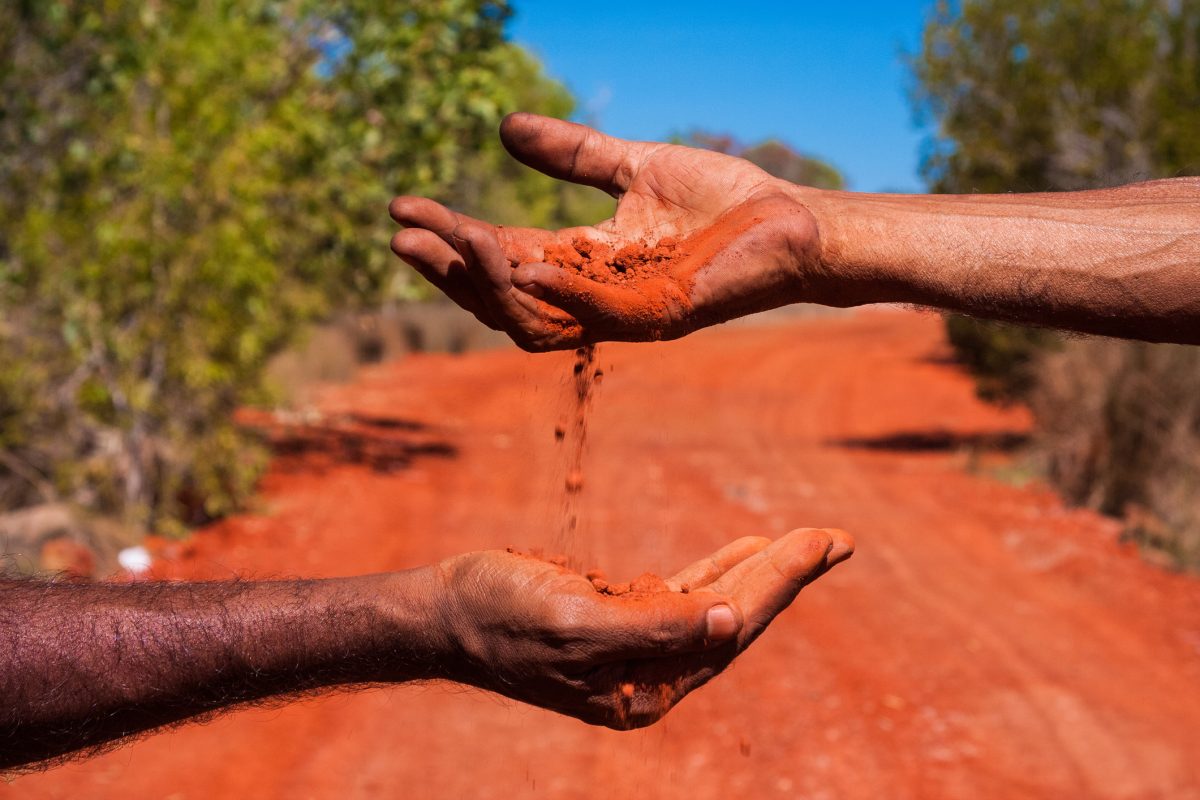 Red dirt being dropped from one hand to another in the Australian bush