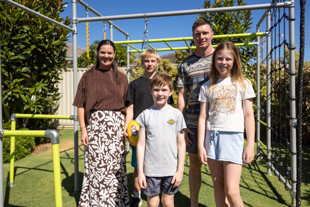 A family standing together in a backyard with a jungle gym behind them