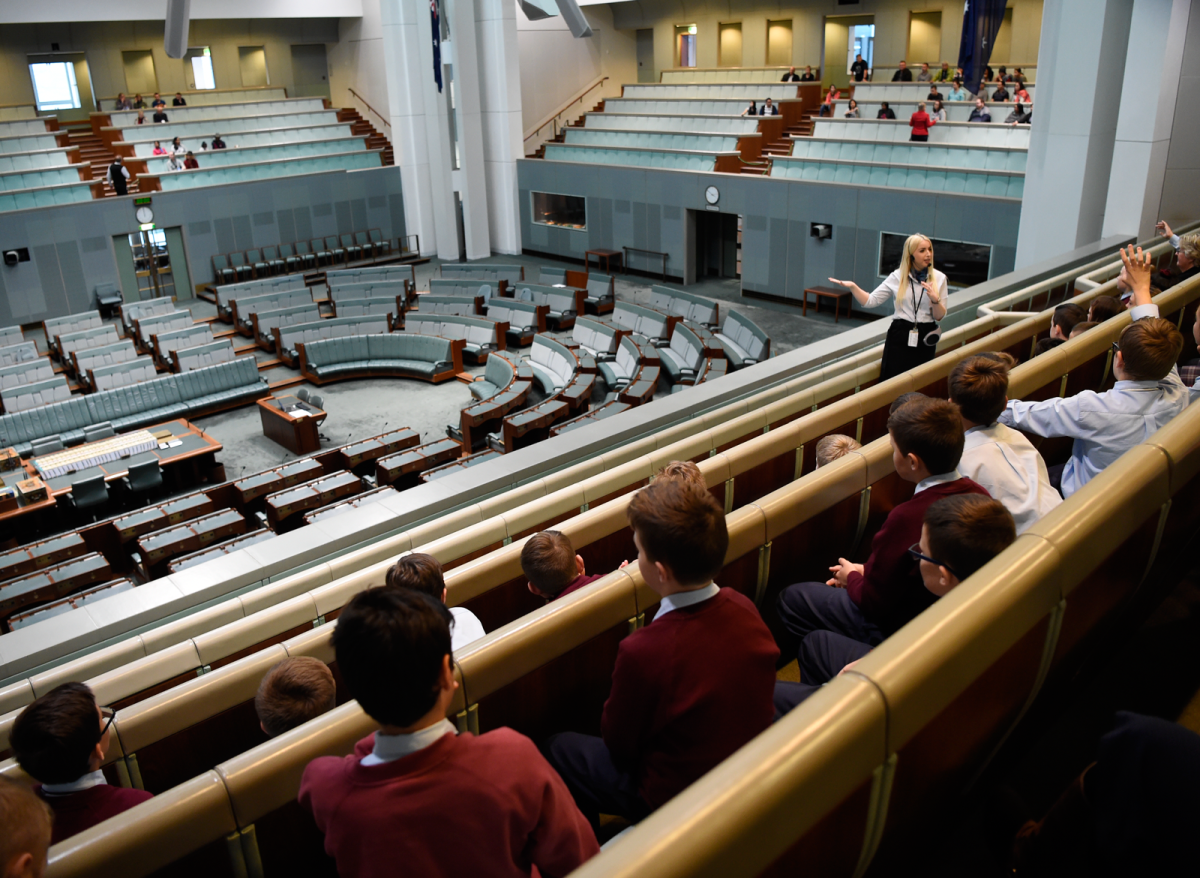 A group of school kids looking at the lower chamber from a viewing gallery, while a tour guide speaks to them.