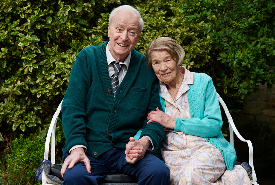 two seated elderly people holding hands