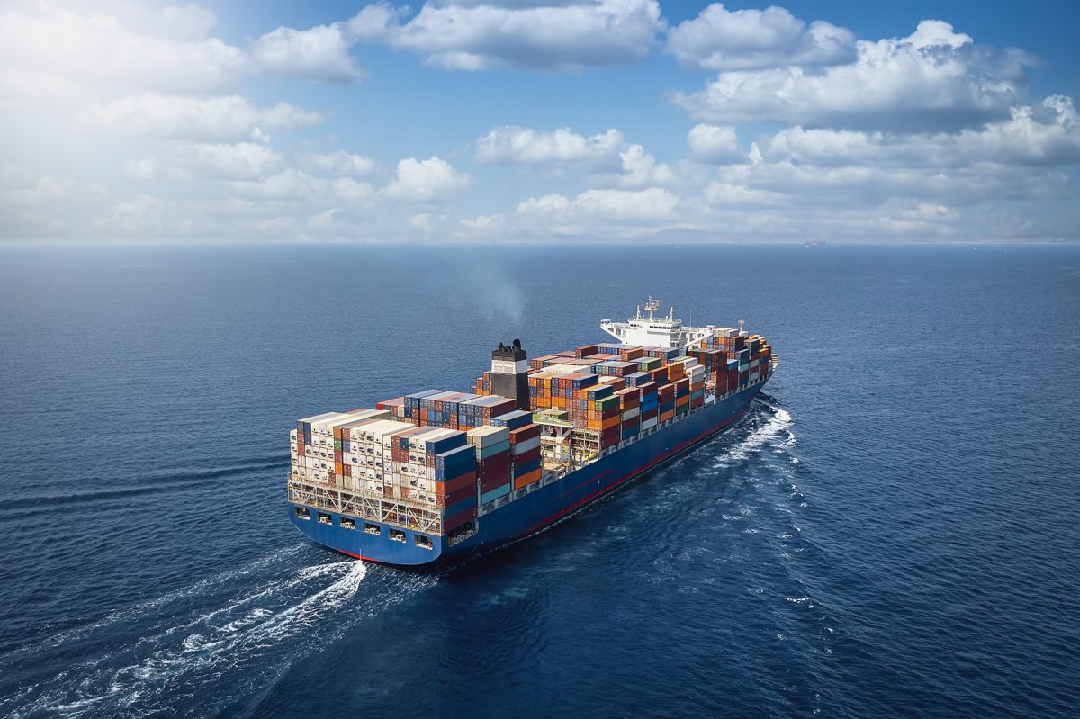 A large container cargo ship travels over calm, blue ocean.