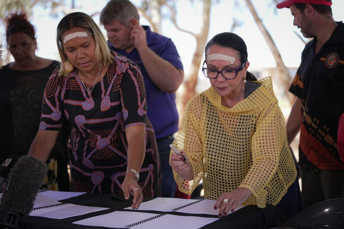 Selena Uibo and Linda Burney signing the Local Decision Making Agreement with Ngurratjuta Aboriginal Corporation members around them.
