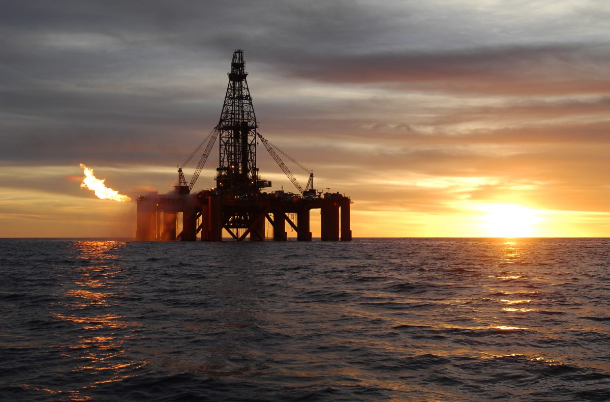 An ocean oil rig flaring natural gas at sunset.