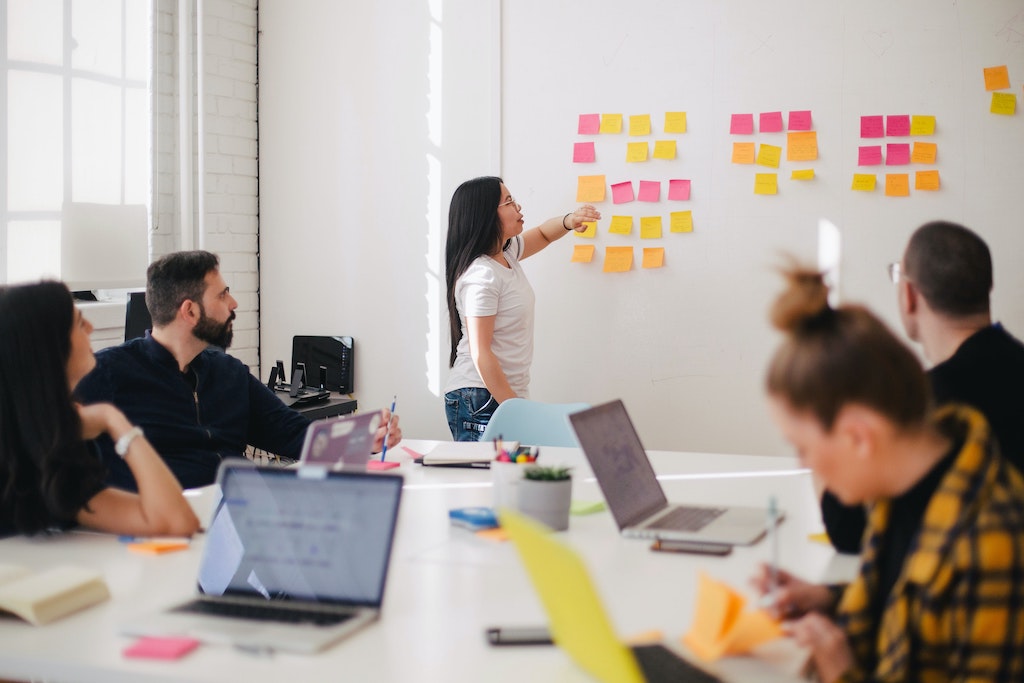 woman at whiteboard and people at laptops listening 