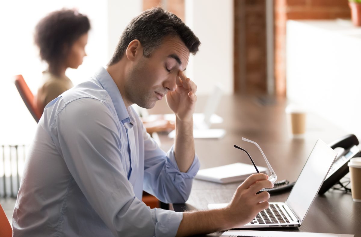 man rubbing his eye while at his laptop