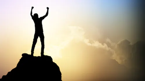 Person with arms outstretched atop a hill