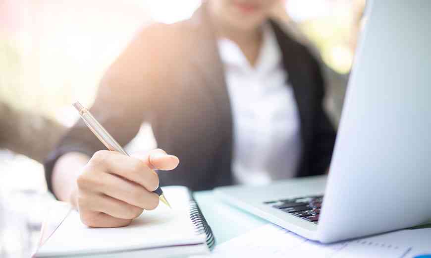 person writing in a notebook on their desk