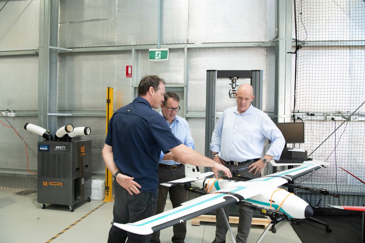 Three men talking as they assess a model drone in a warehouse.