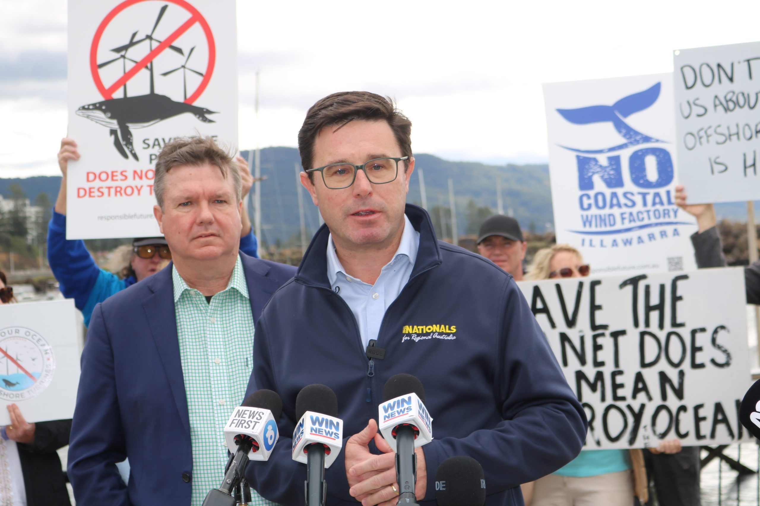 man holding a press conference in front of protesters