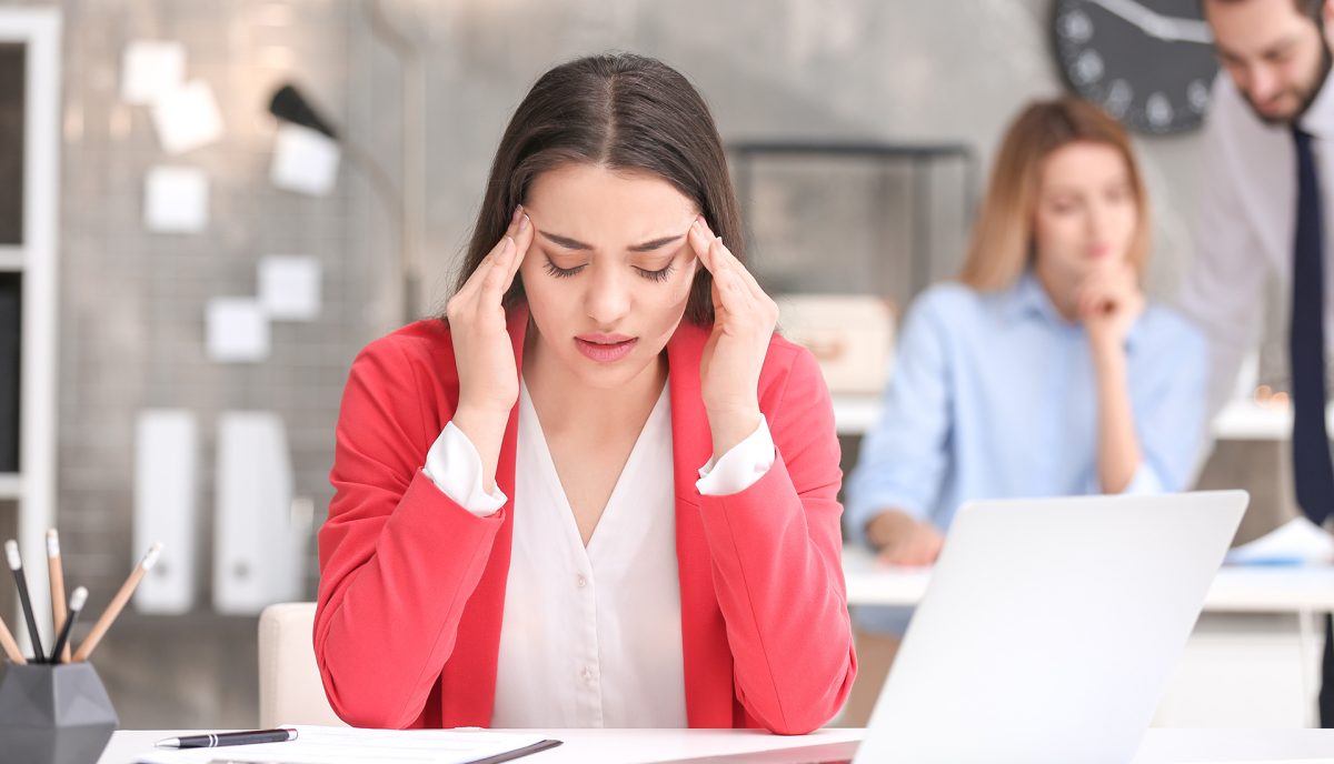 woman at her office desk with her hands at her temples 