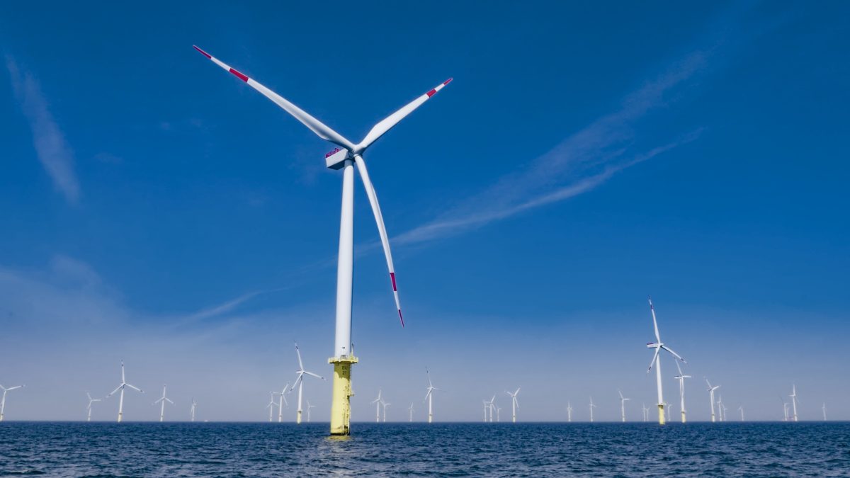 Wind turbines spinning in sea against blue sky.