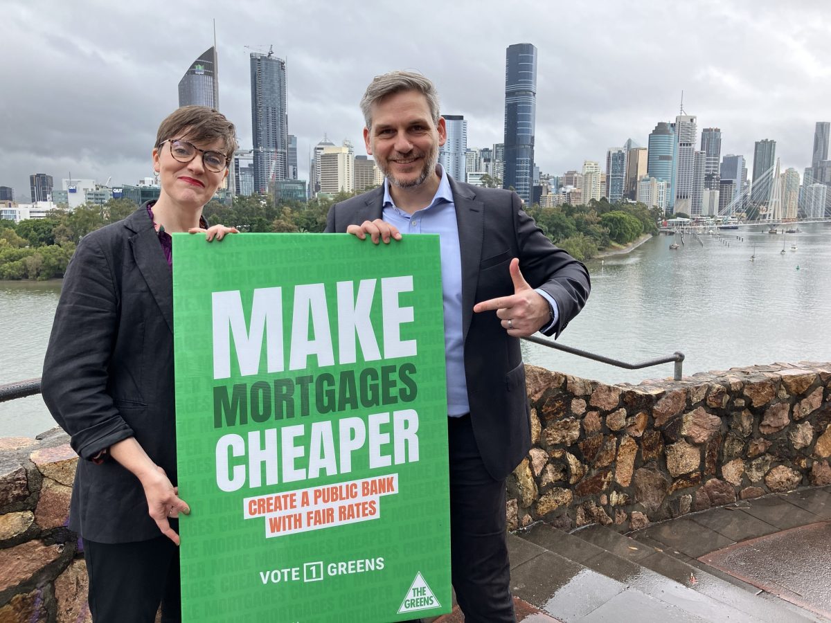 Two politicians holding up a sign saying 'MAKE MORTGAGES CHEAPER' with the Brisbane river in the background.