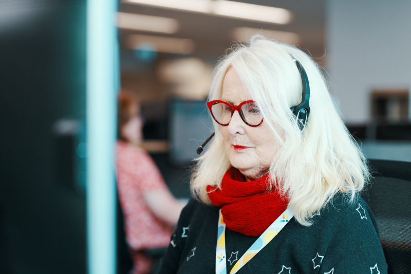 Older woman with a headset on at her desk in an office