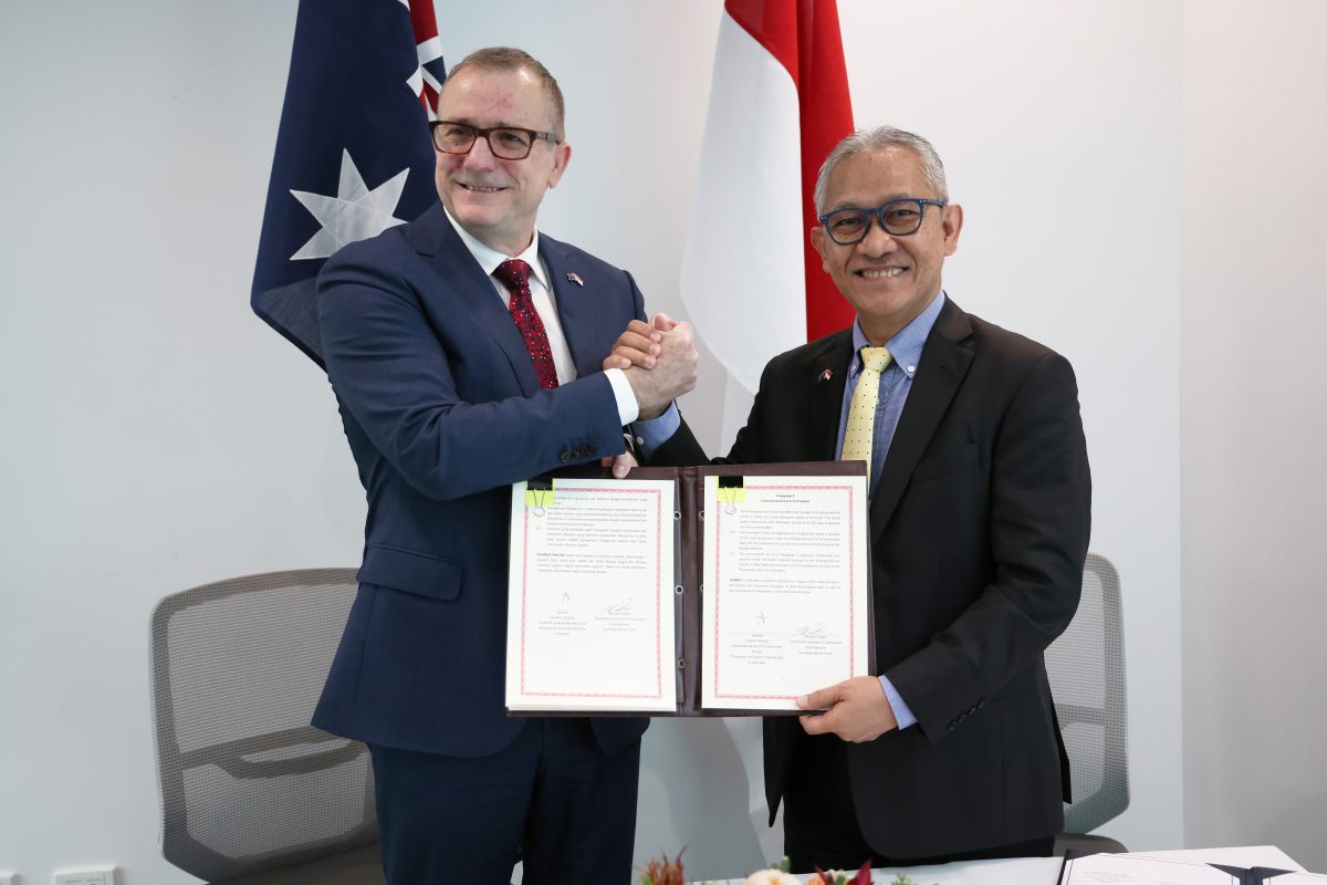 two suited men shaking hands and displaying a signed agreement