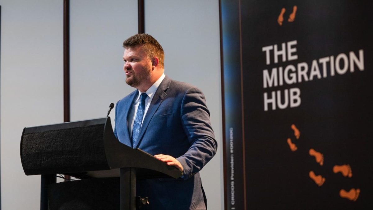 man speaking from a lectern in front of a sign