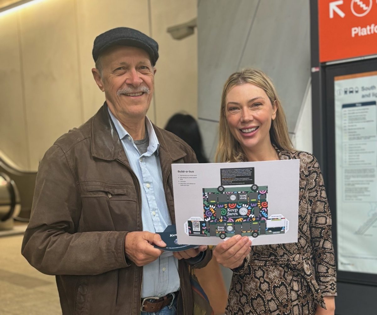 An old man and young woman at a public train station holding up a union sign.