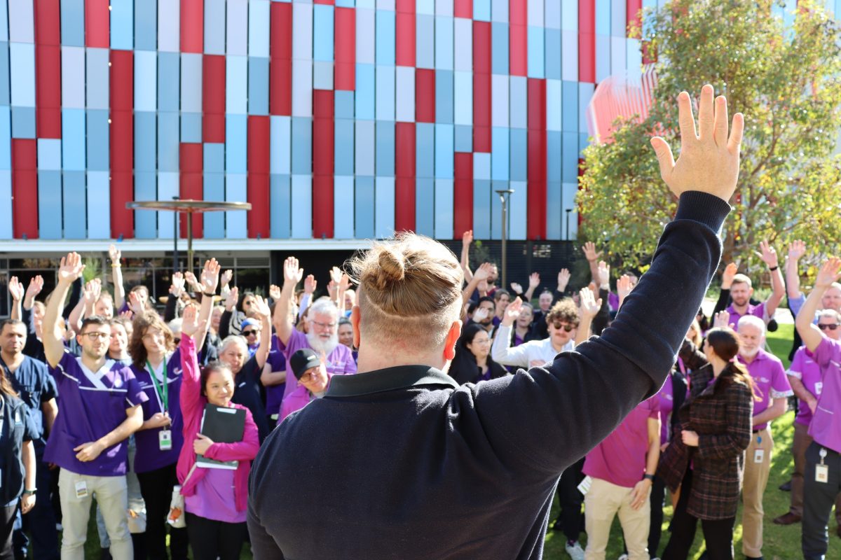 Hospital pharmacists together at a rally with one hand raised up.