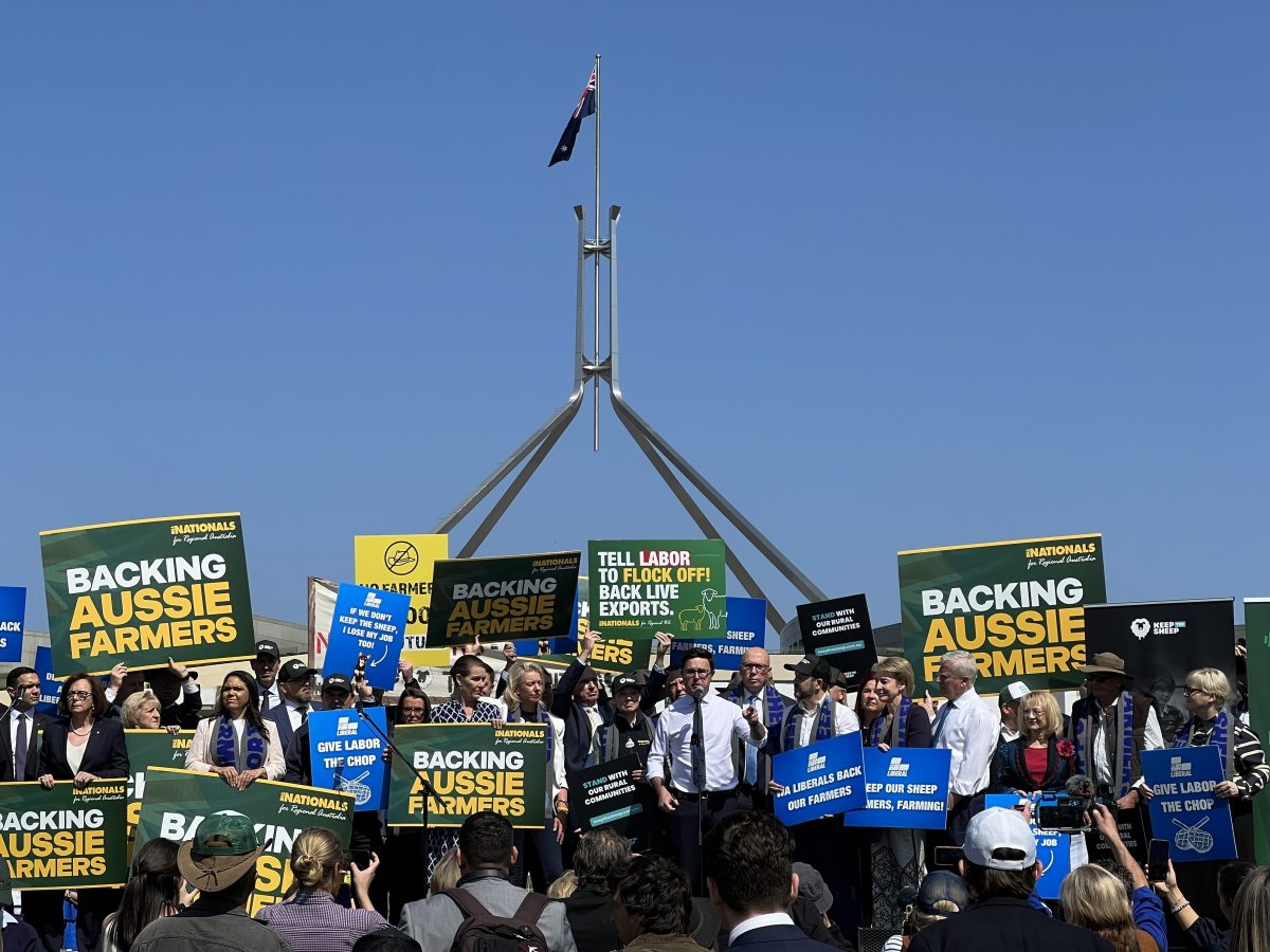 A group of Liberal and National party politicians stand together on a platform before Parliament House with signs in support of farmers.