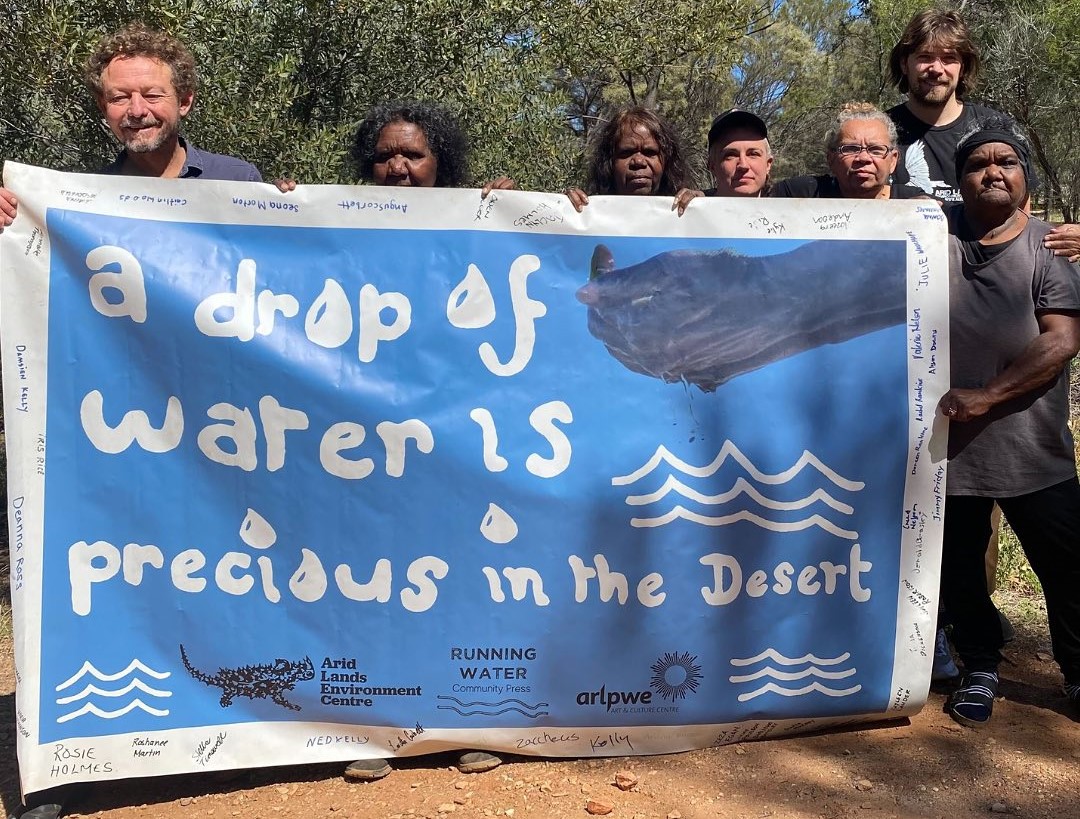 A group of people holding up a blue sign reading 'a drop of water is precious in the Desert'.