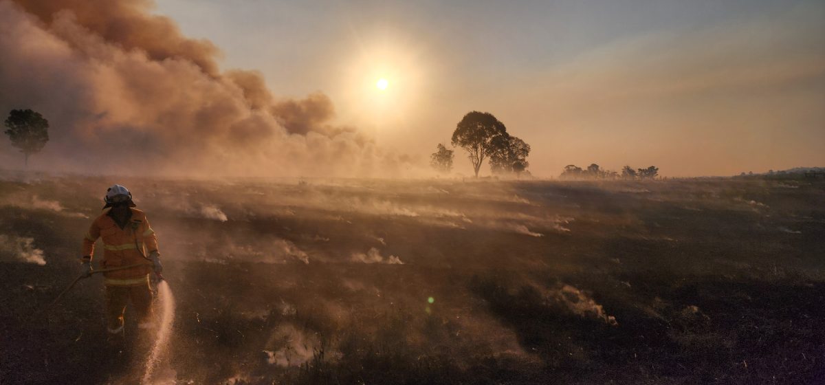 Firefighter spraying water on a plain with the sun high in the sky