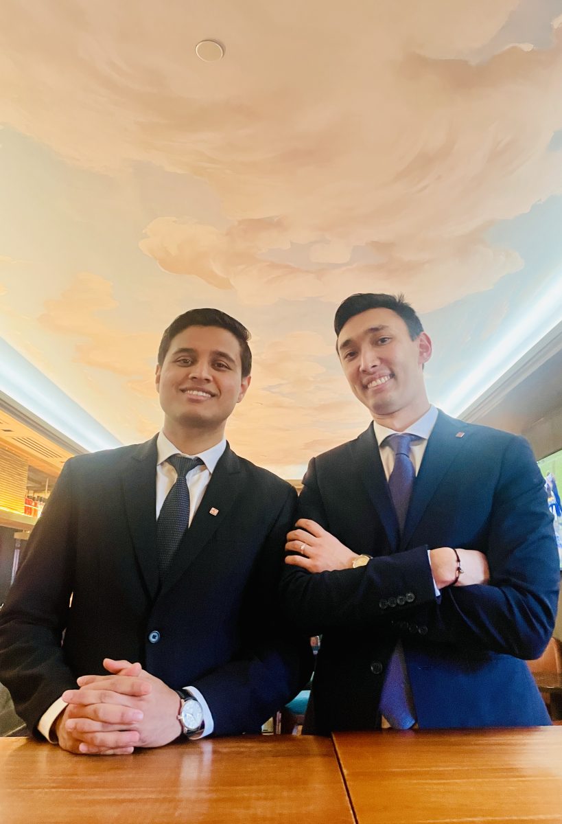 two suited men in a hotel, with a ceiling mural above them