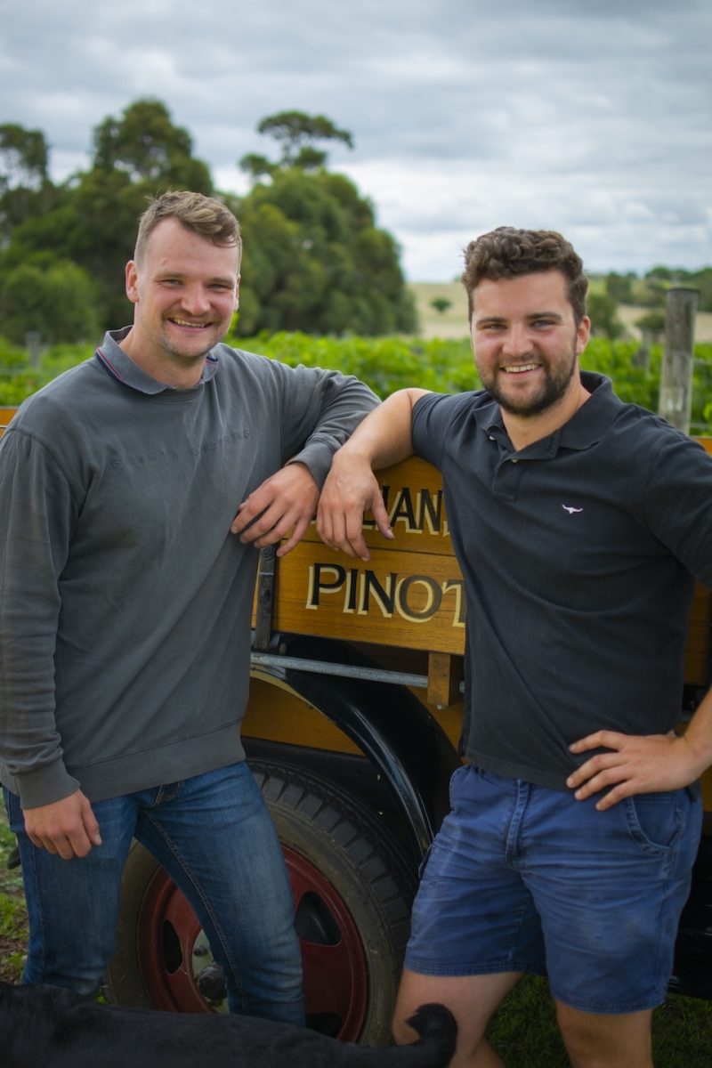 two men leaning against an old truck at a vineyard