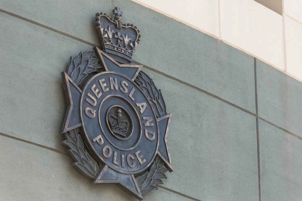 Metal QLD Police insignia on a concrete wall.