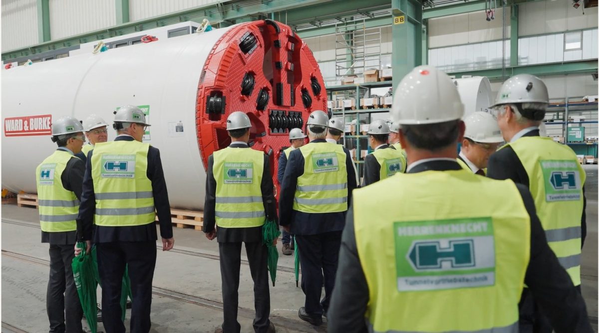 A group of people with high vis jackets and hard hats standing around a tunnel boring machine.